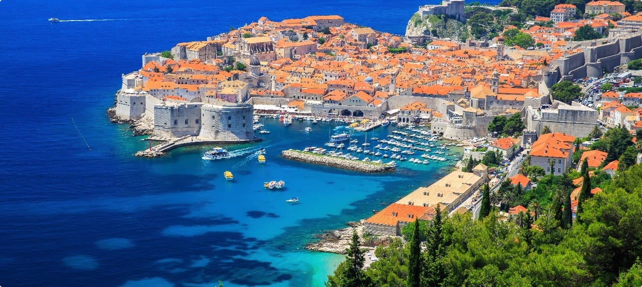 Historic waterfront of a Croatian coastal town with orange-roofed stone buildings along a calm harbor