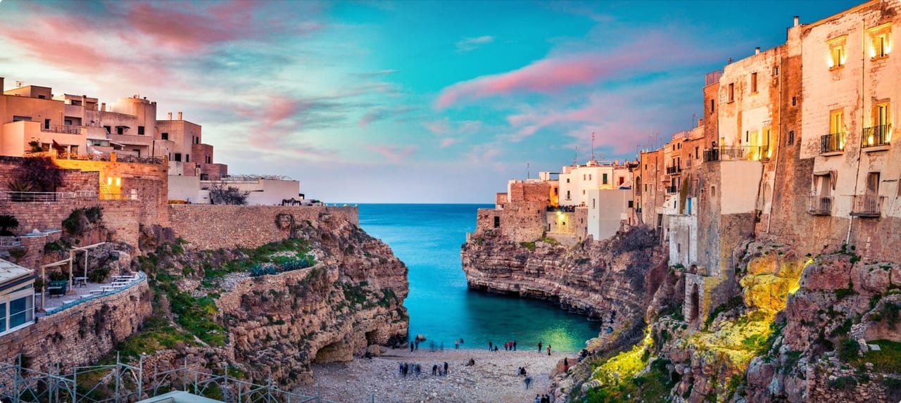 Sunset over the cliffside village of Polignano a Mare, Italy with ancient stone buildings overlooking a sheltered turquoise cove