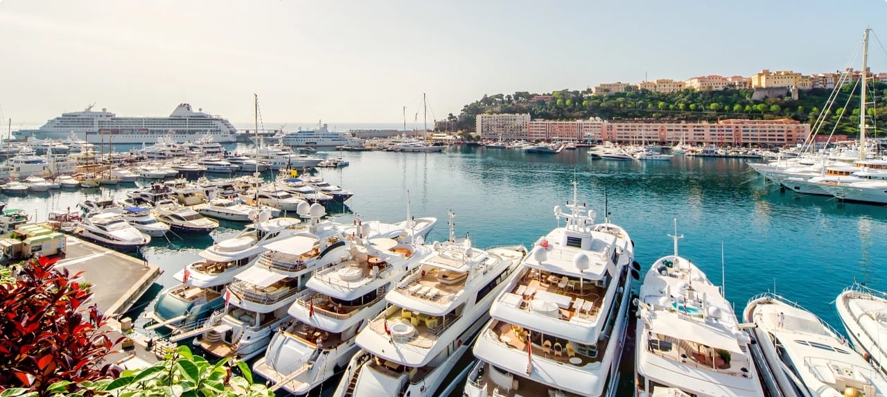 Port Hercule marina in Monaco filled with rows of luxury yachts against a backdrop of Mediterranean cliffs
